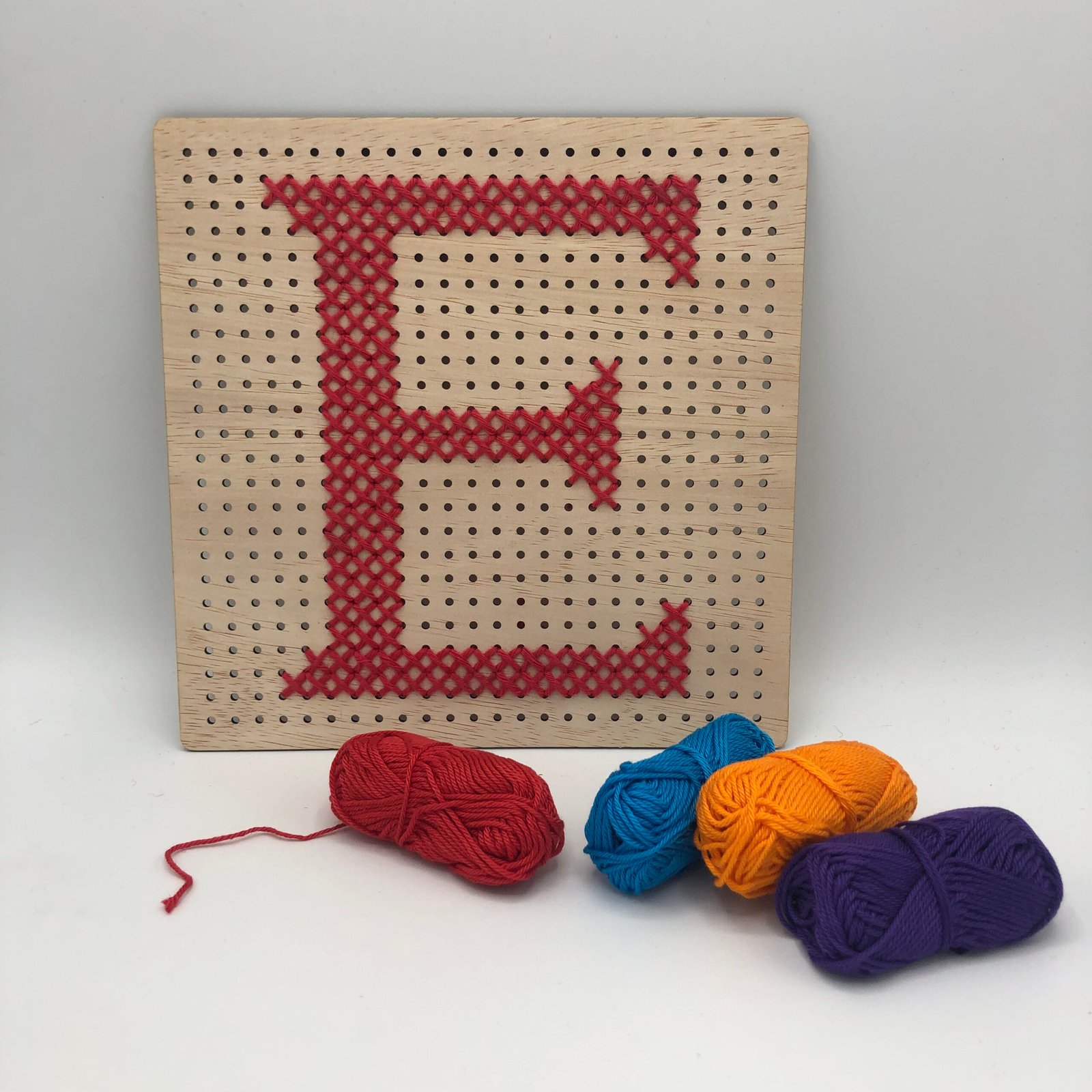 Houten bord met geborduurde letter E in rood garen, creatief DIY borduurpakket van MaakTzelf.