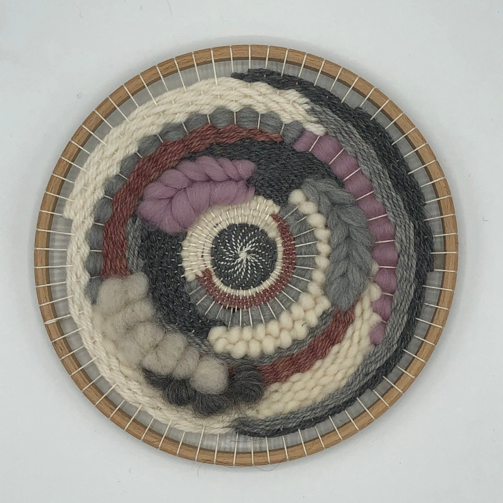 Rond geweven kunstwerk in aardetinten met grijs, crème en zacht paars, gemaakt met DIY weefpakket van MaakTzelf.