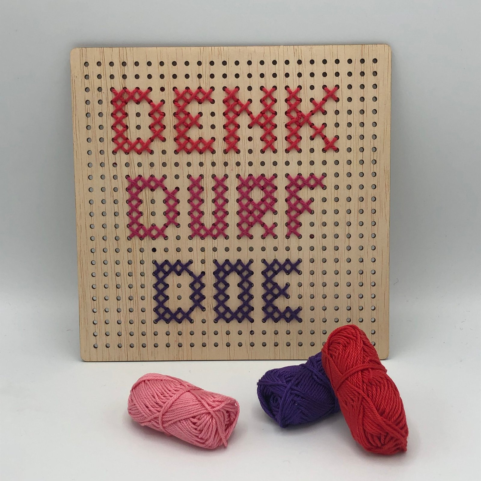 Houten borduurpakket met de tekst ‘Denk Durf Doe’ in rood en paars garen, creatief DIY knutselproject van MaakTzelf.
