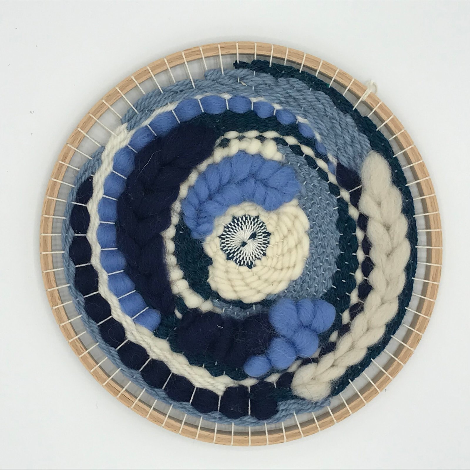 Ronde geweven wanddecoratie in blauw en crème tinten, gemaakt met het weefpakket van MaakTzelf.