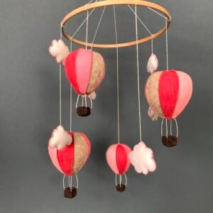 Mobiel voor in de kinderkamer bestaande uit een houten ring met daaraan figuren van wolvilt hangend. Er hangen 4 luchtballonnen in roze tinten en 6 witte wolkjes aan, die met de hand zijn genaaid.