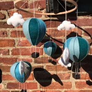 Mobiel van een houten ring met daaraan 4 blauwe luchtballonnen en 6 witte wolkjes van wolvilt. Op de achtergrond een muur van bakstenen