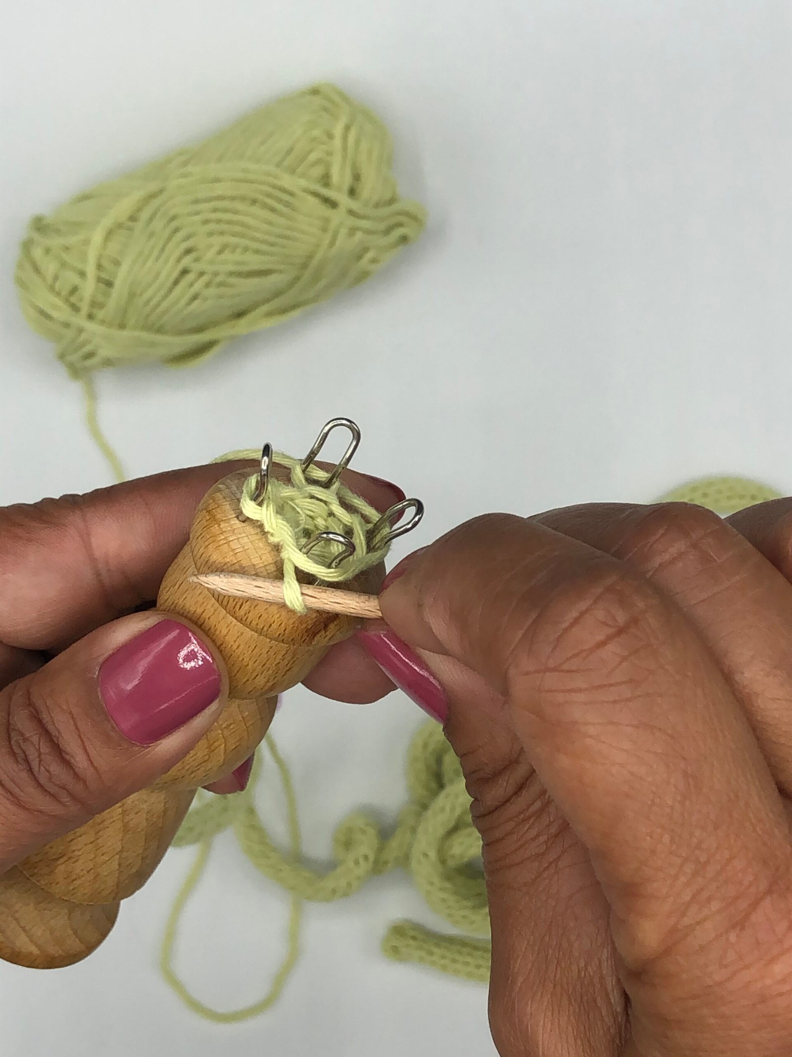 Close-up van handen die punniken met lichtgroen katoengaren op een houten punnikklosje.