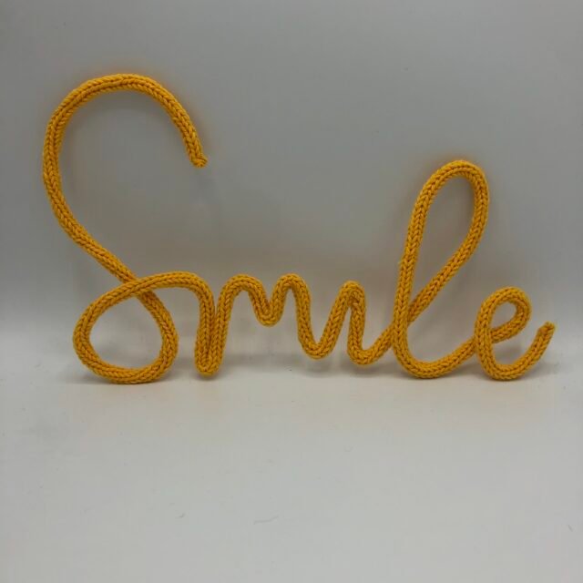 Geel gepunnikt woord ‘Smile’, handgemaakt met katoen, creatief DIY punnikpakket van MaakTzelf.