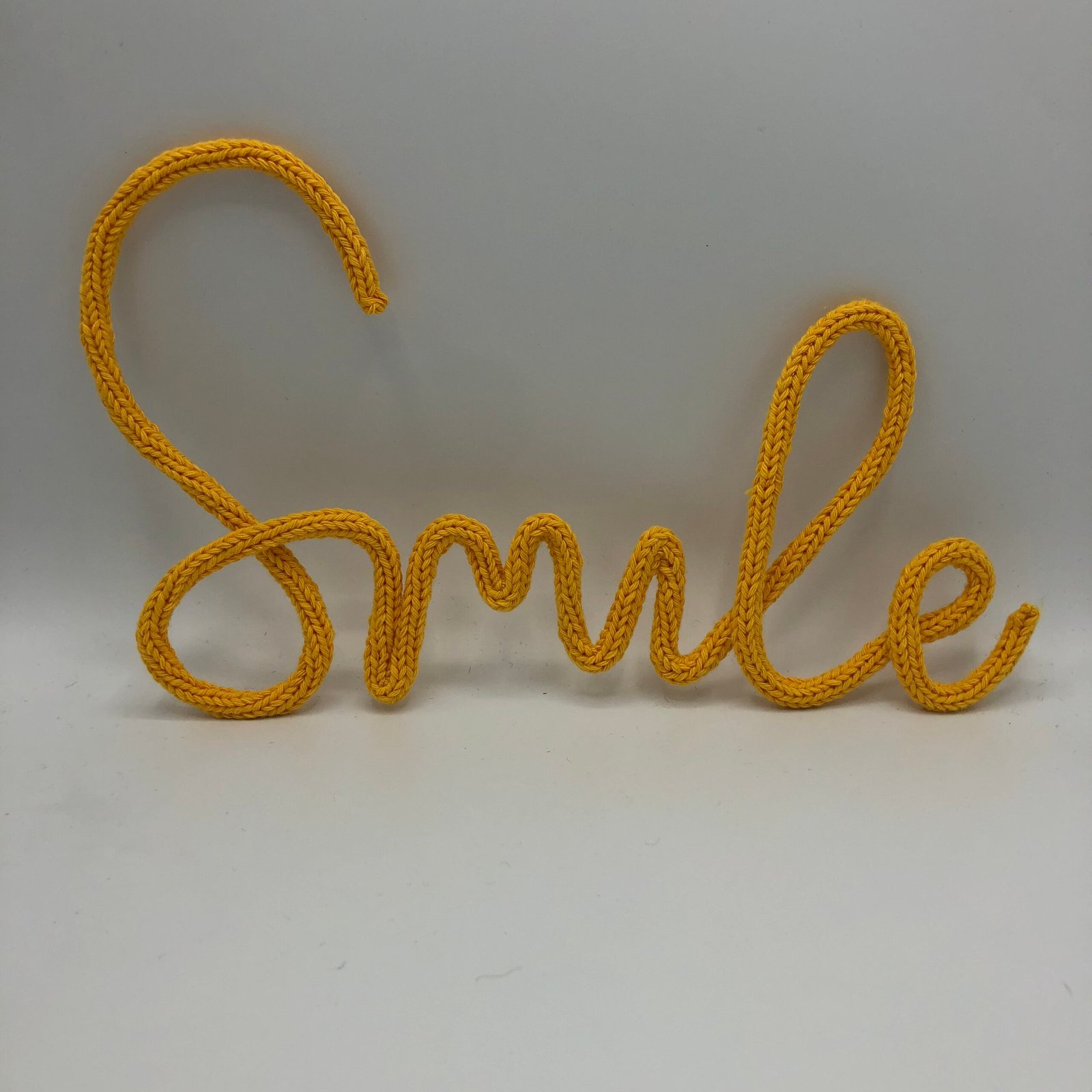 Geel gepunnikt woord ‘Smile’, handgemaakt met katoen, creatief DIY punnikpakket van MaakTzelf.